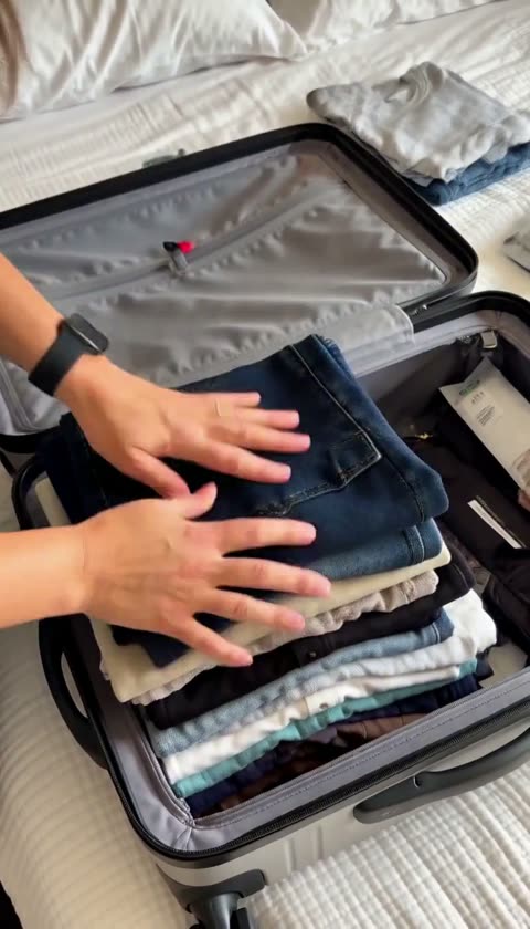 AI-generated hands smoothing folded clothes inside an open suitcase